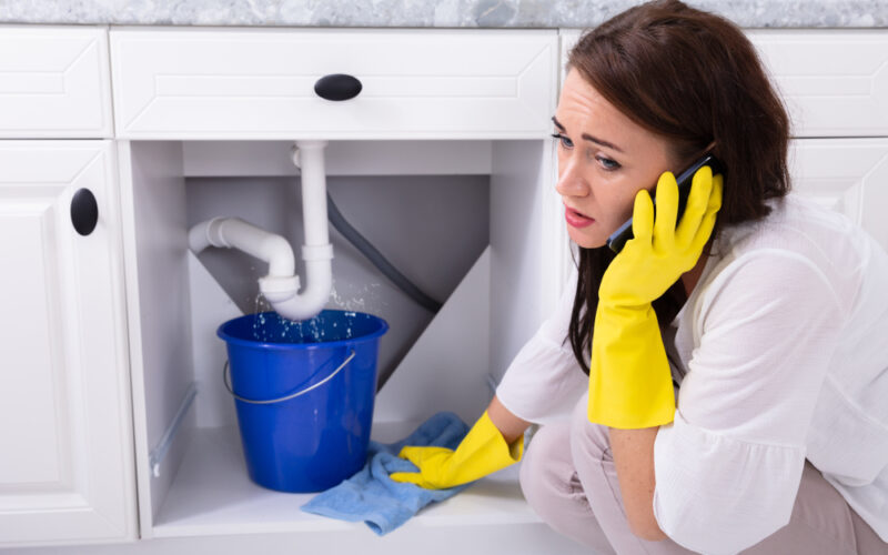 Sad,Young,Woman,Calling,Plumber,In,Front,Of,Water,Leaking